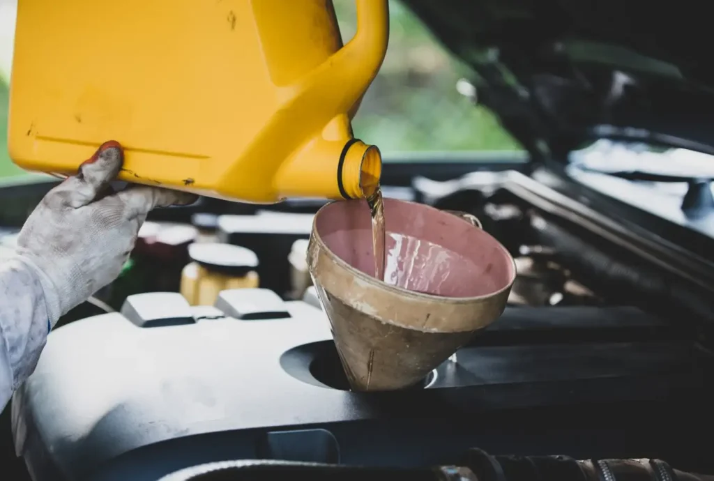 Pouring engine oil into a car engine using a funnel. A gloved hand holds a yellow container.