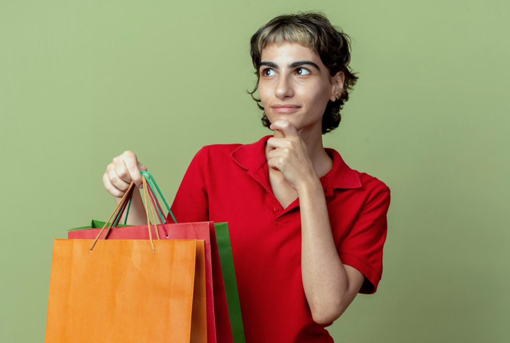 Person in a red shirt holding colorful shopping bags against a green background, looking thoughtful.