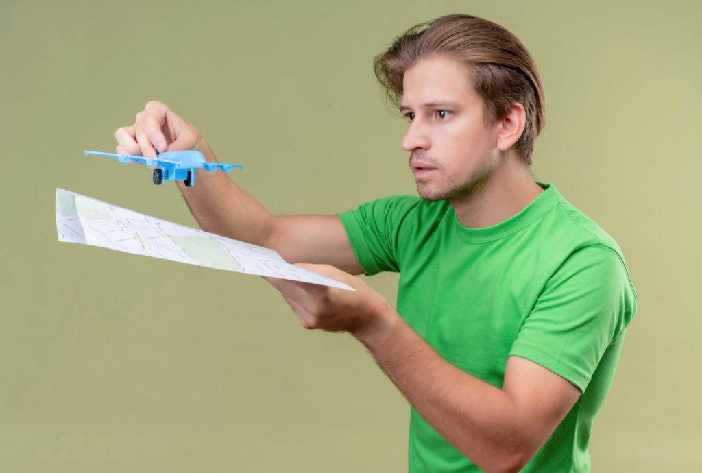 Man in green shirt holds a blue toy plane and a paper map, appearing focused and thoughtful against a light green background.