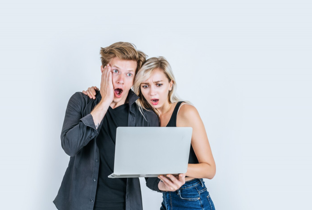 Two individuals look surprised while viewing a laptop screen, expressing shock or disbelief.
