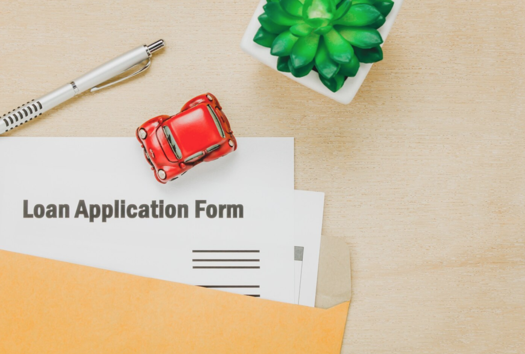 Loan application form with pen, toy car, and green succulent on a wooden desk.