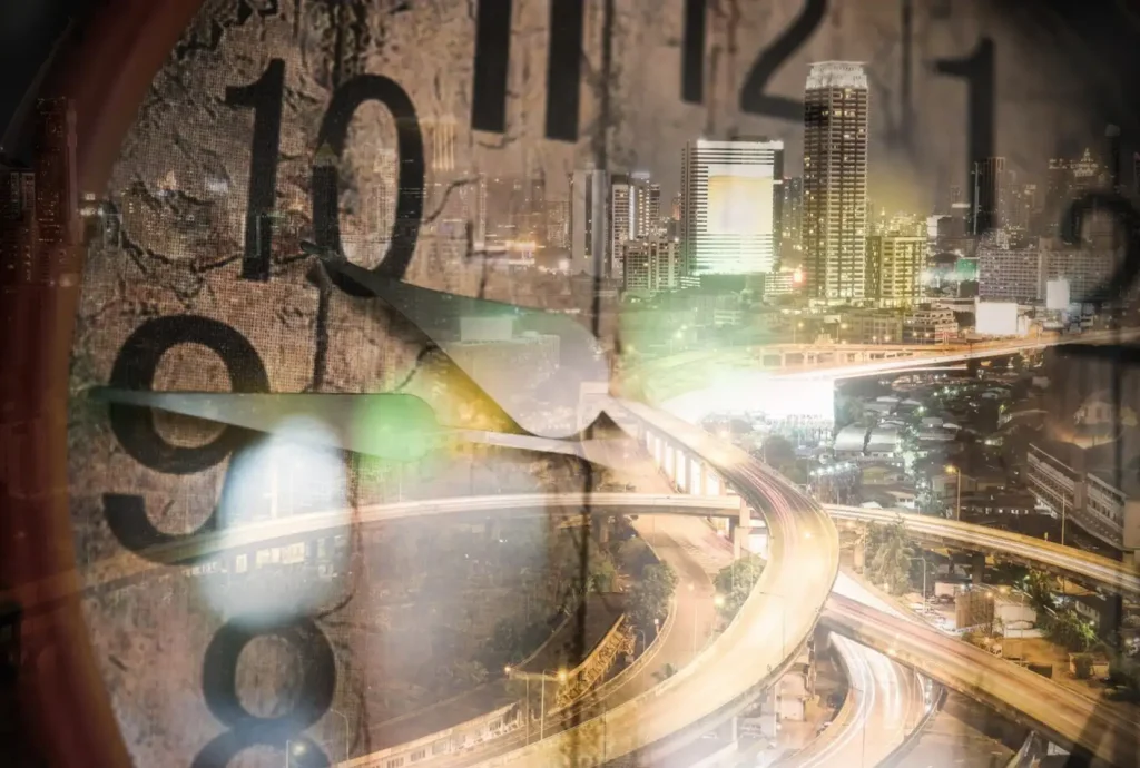 Blended image of a clock face showing 10:10 with a vibrant cityscape featuring skyscrapers and highways at night.