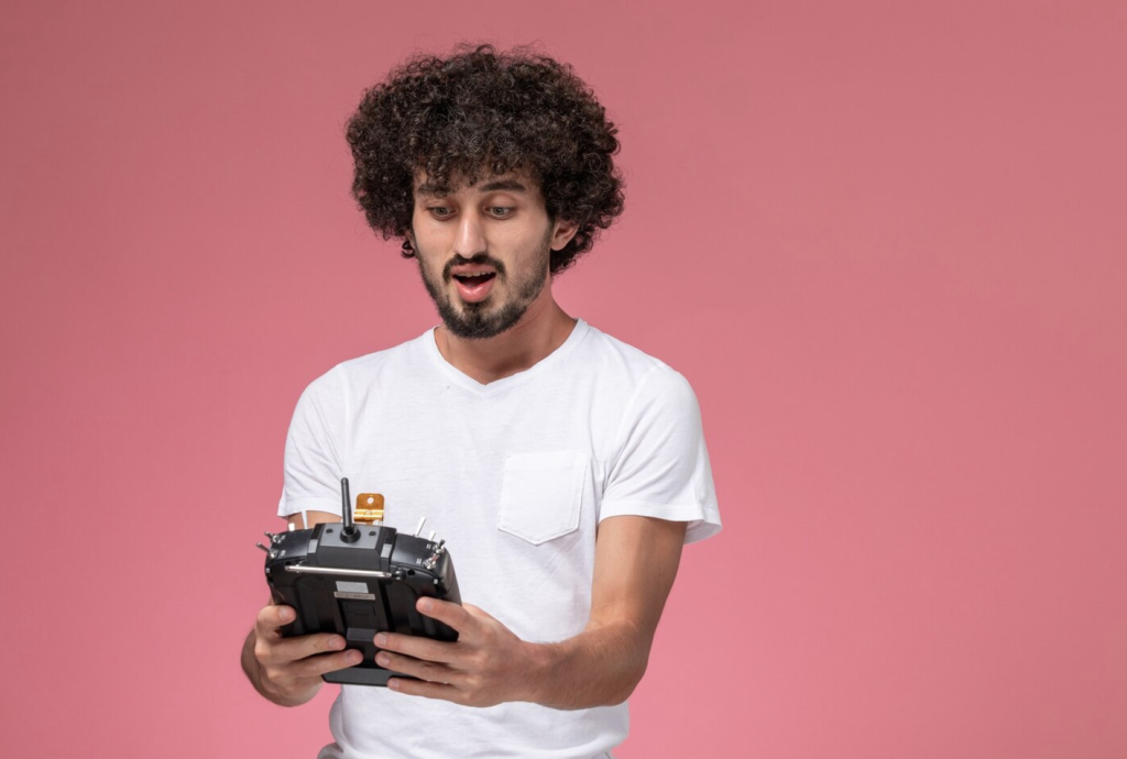Man in a white shirt holding a remote control, looking surprised, against a pink background.