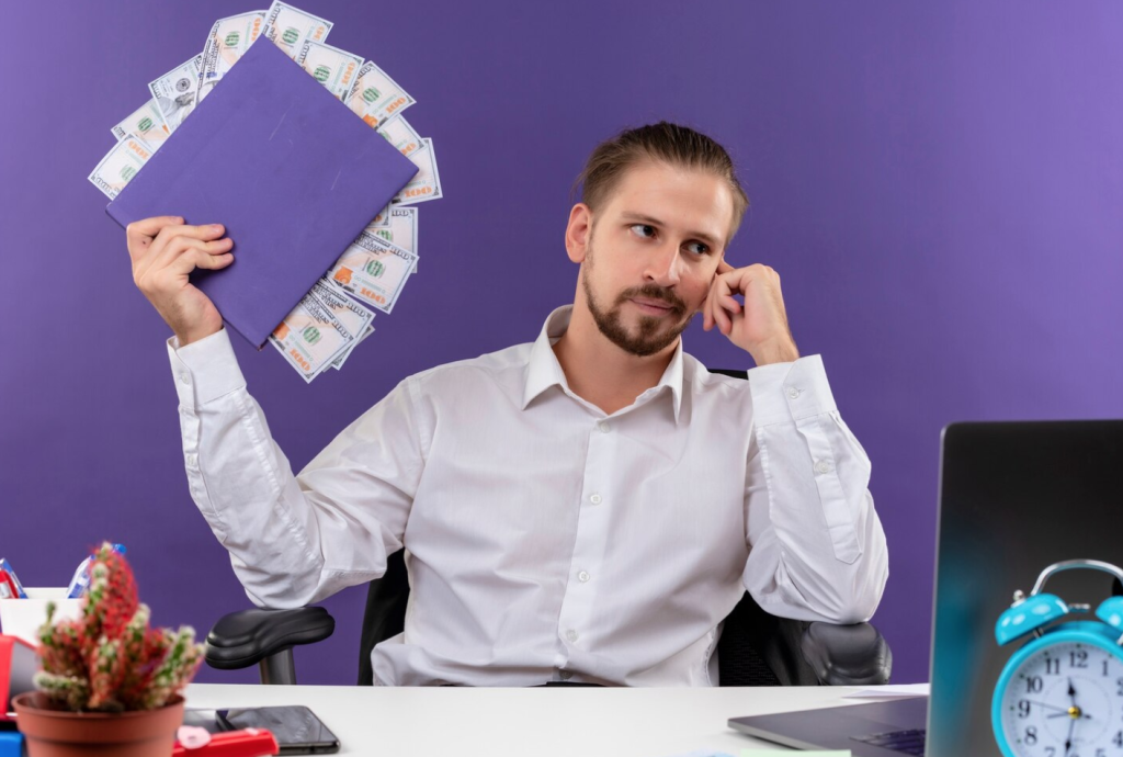 Man in white shirt holding a folder with money, sitting at a desk with a laptop and clock, purple background.