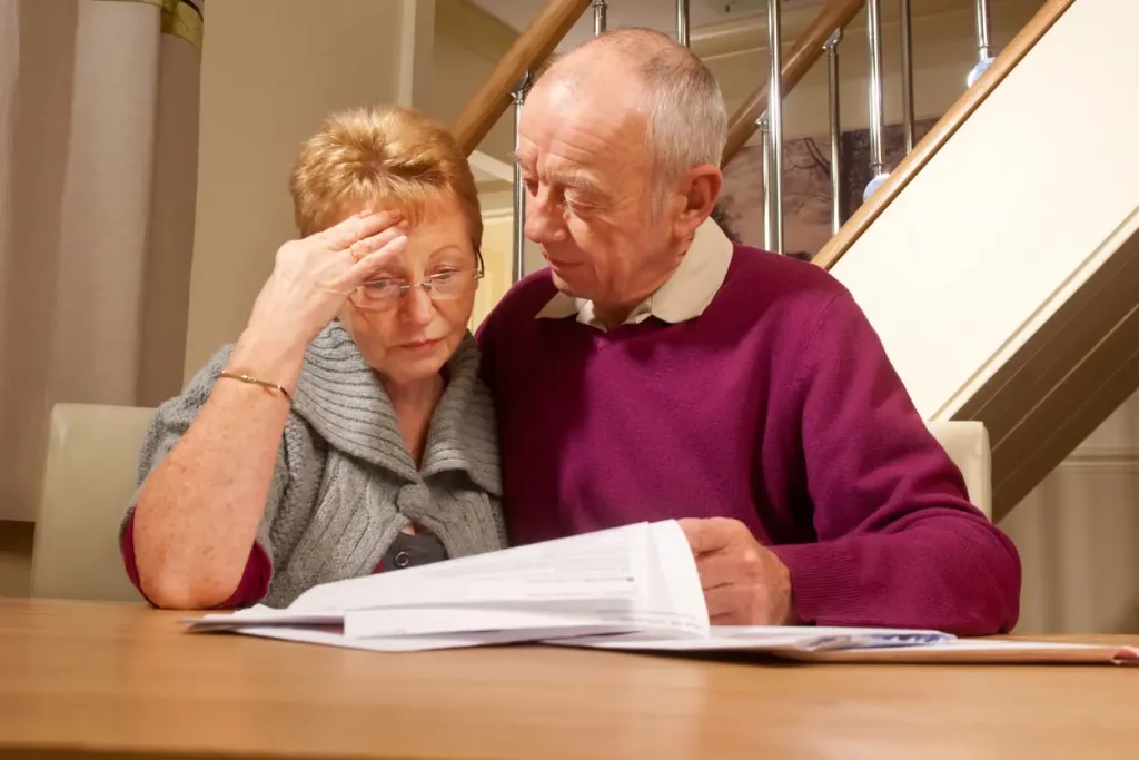 Elderly couple reviewing documents at a table, looking concerned and thoughtful.