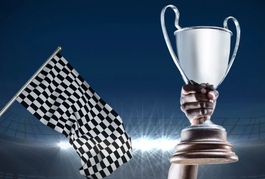 A hand holds a silver trophy above a checkered flag with stadium lights in the background.