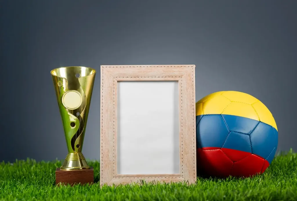 Trophy, blank photo frame, and Colombian-themed soccer ball on grass with gray background.