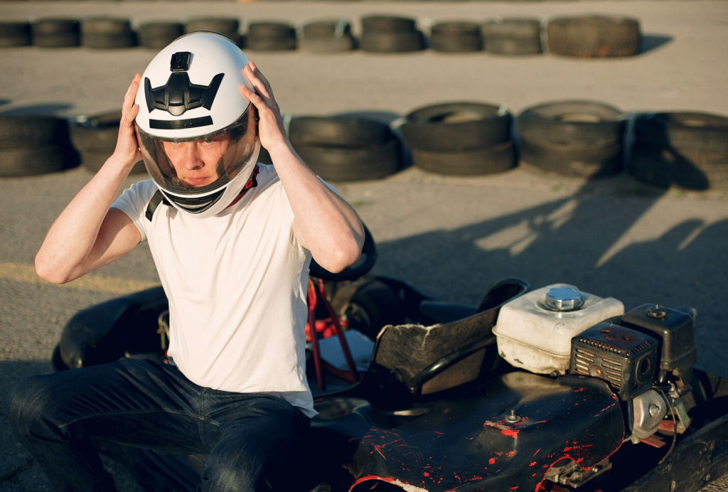 Person in white helmet preparing to drive a go-kart, with stacked tires in the background.