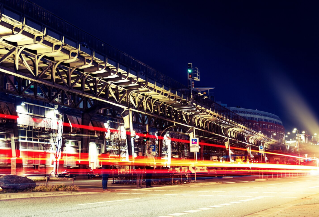 Nighttime city street scene with light trails under a modern elevated structure, capturing motion and urban architecture.