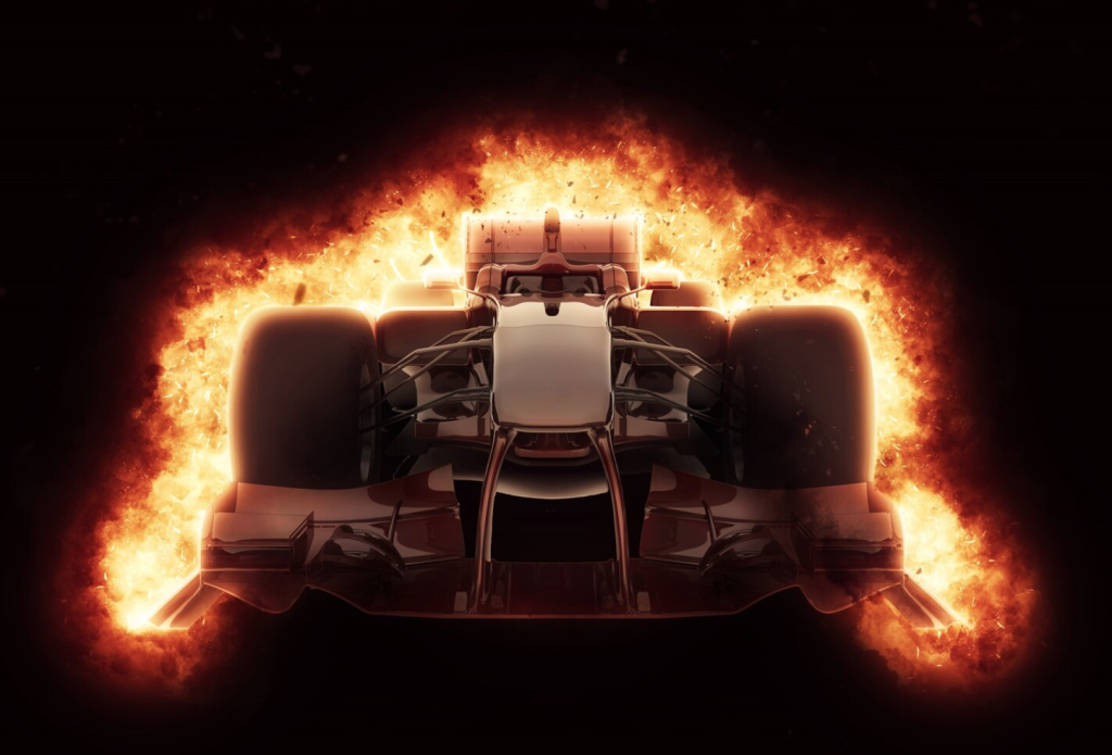 Front view of a Formula 1 car engulfed in vibrant flames against a black background.