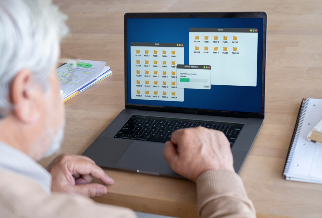 Person copying files on a laptop, displaying folders and a progress bar, with notebooks on the table.