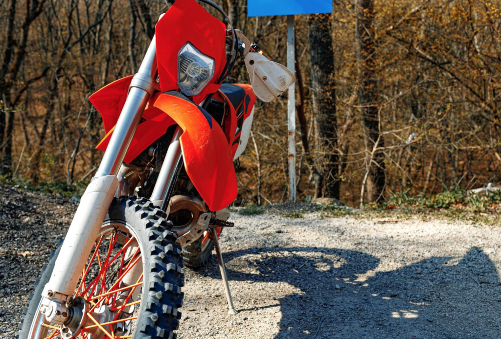 Red dirt bike parked on a gravel path in a forested area during autumn.