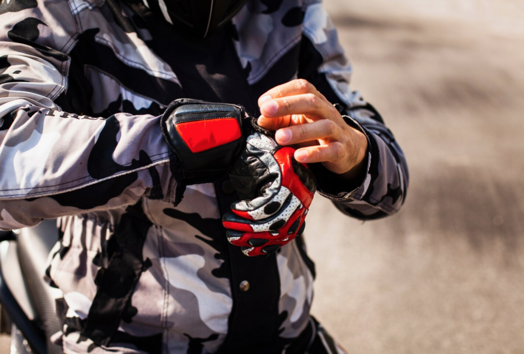 Person adjusting red and black motorcycle gloves, wearing a camouflage jacket.