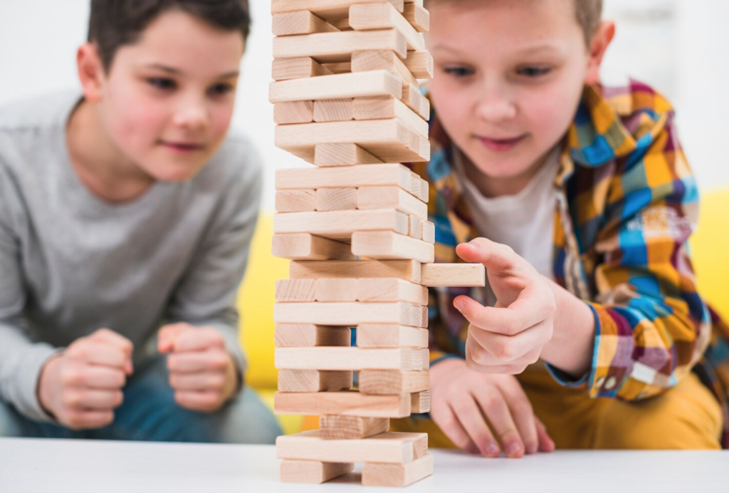 Two children focus on a Jenga tower as one carefully pulls a block, showcasing concentration and dexterity.
