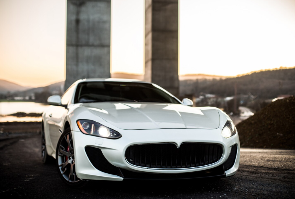 White sports car parked outdoors at sunset, with hills and industrial structures in the background.