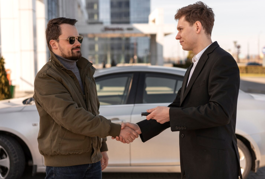 Two men shaking hands in front of a white car, one handing over car keys, symbolizing a car sale or agreement.